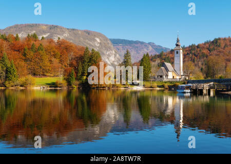 Chaud sur le lac de Bohinj dans des couleurs automnales et l'église catholique de Saint-Jean-Baptiste, les Alpes Juliennes, en Slovénie. La religion, voyage, visite Banque D'Images