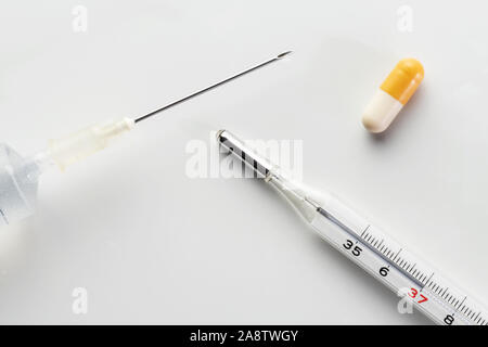 Seringue médicale, thermomètre à mercure et comprimé capsule isolé sur fond blanc. La vaccination, grippe, médecine, pharmacie, pédiatrie et choix Banque D'Images