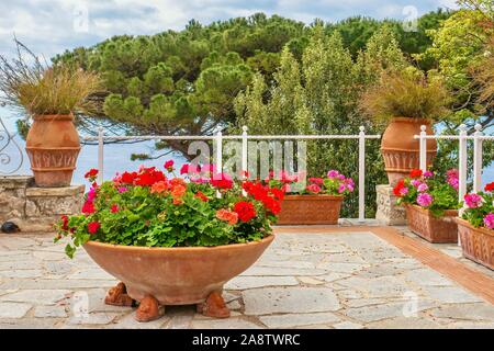 Un jardin d'été par la mer. Géraniums colorés en pots de terre cuite sur une terrasse en pierre surplombant la mer Méditerranée à l'Italie. Banque D'Images