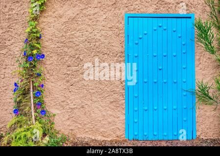 Rue d'un bâtiment rustique simple façade dans le Maroc rural, avec une porte en bois bleu, une texture mur extérieur, et des plantes grimpantes. Banque D'Images
