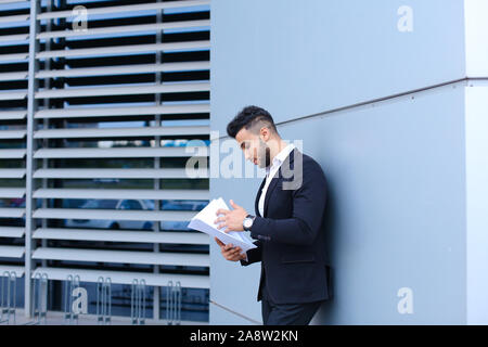 Jeune homme d'affaires asiatique détient et estime, lit et trie des papiers, se trouve à proximité de mur de centre d'affaires. Banque D'Images