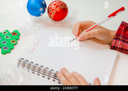 Cher Père Noël Lettre, carte de Noël. Un enfant tenant un stylo écrit sur une feuille blanche sur un fond de bois avec décor du Nouvel An. Rêves d'enfant à propos de Banque D'Images