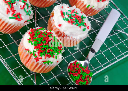 Red Velvet cupcakes de Noël fait maison avec du fromage à la crème glaçage blanc surmonté de maison de couleur rouge vert et blanc paillettes. Banque D'Images