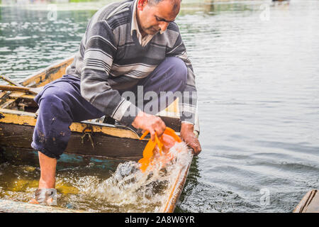 Un vieil homme retire de l'eau qui est entrée dans la bateau cassé. Banque D'Images