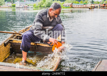 Un vieil homme retire de l'eau qui est entrée dans la bateau cassé. Banque D'Images