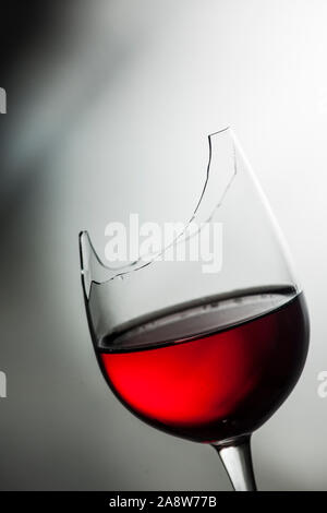 Portrait du haut de la rupture d'un verre de vin rempli de vin rouge en face de background avec gradient clair et foncé. Banque D'Images