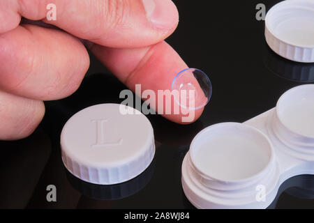 Lentilles de contact toriques sur le bout du doigt avec étui blanc et le chapeau - composition sur fond réfléchissant noir. Banque D'Images