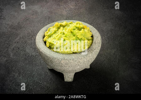 Le guacamole dans un molcajete, avocat mexicain dans la mortier traditionnel en pierre, sur un fond noir Banque D'Images