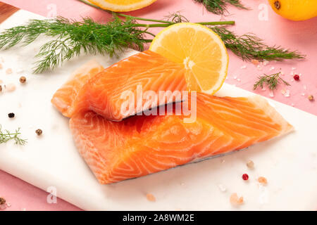 Tranches de saumon au citron et aneth, close-up avec sel et poivre, la cuisson du poisson, sur un fond rose Banque D'Images