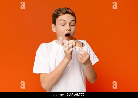 Teenage guy bénéficiant d'eclair au chocolat, fond orange Banque D'Images