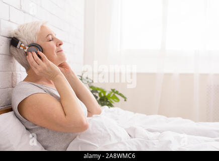 Senior lady tranquille à écouter un livre audio au lit Banque D'Images
