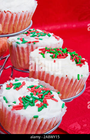 Velours rouge maison de vacances de Noël cupcakes garnis d'un fromage à la crème glaçage blanc avec rouge vert et blanc couleur paillettes. Banque D'Images