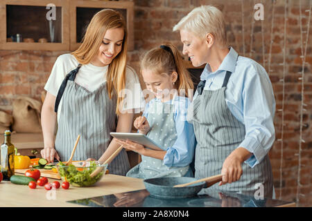 Petite fille montrant la maman et grand-mère de nouvelles recettes sur tablette Banque D'Images