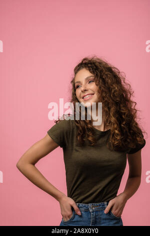 Jolie fille avec des cheveux bouclés posing in studio à la caméra de isolé sur fond rose Banque D'Images
