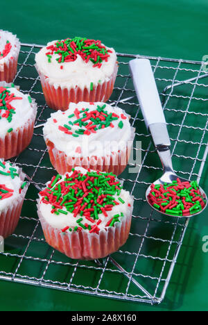 Noël velours rouge maison cupcakes avec glaçage au fromage à la crème de couleur blanche surmontée de rouge vert et blanc coloré paillettes. Banque D'Images