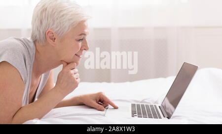 Pensive woman la navigation sur ordinateur portable, dans mon lit Banque D'Images