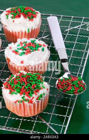 Noël velours rouge maison cupcakes avec glaçage au fromage à la crème de couleur blanche surmontée de rouge vert et blanc coloré paillettes. Banque D'Images