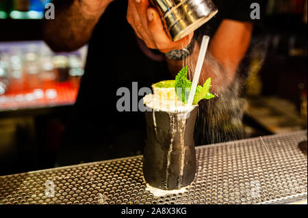 Bartender pouring mains sucre glace sur le lac perdu avec cocktail à l'intérieur des feuilles moyenne nuit bar à cocktails, Close up Banque D'Images