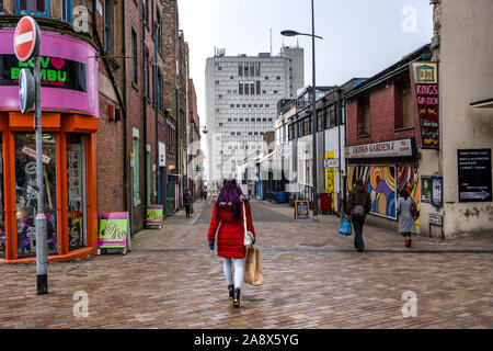 Une jeune femme dans un manteau rouge marche dans le centre-ville vers le vieux bâtiment BT portant un sac en papier brun Primark Banque D'Images