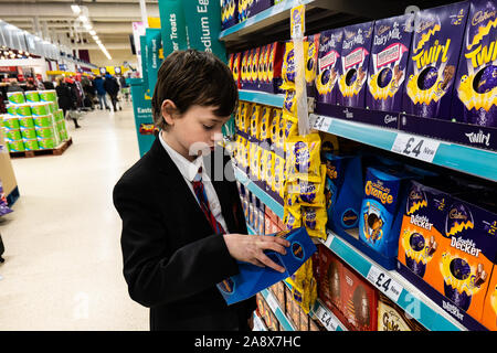 Un beau jeune garçon de l'école avec le TDAH, l'Autisme, syndrome d'Aspergers ressemble, parcoure, examine certaines des oeufs de Pâques dans le supermarché Tesco store local supplémentaire Banque D'Images