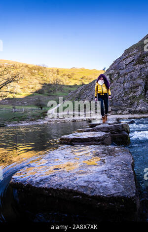 Une jolie jeune femme athlétique passe au-dessus de la célèbre Dovedale stepping stones, garder son équilibre sur les roches glacées, National Trust, Peak District Banque D'Images