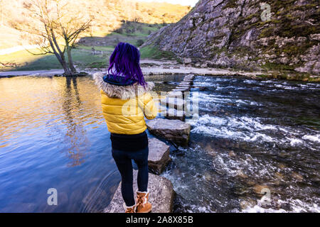 Une jolie jeune femme athlétique passe au-dessus de la célèbre Dovedale stepping stones, garder son équilibre sur les roches glacées, National Trust, Peak District Banque D'Images