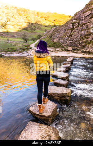 Une jolie jeune femme athlétique passe au-dessus de la célèbre Dovedale stepping stones, garder son équilibre sur les roches glacées, National Trust, Peak District Banque D'Images