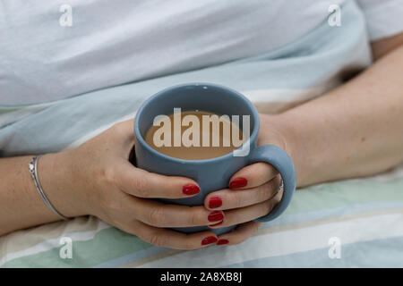 La femme est en train de boire le café du matin au lit Banque D'Images