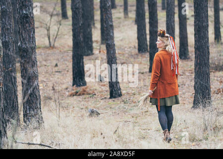 Jeune femme blonde caucasienne dans une couronne avec les feuilles d'automne balade dans la forêt de pins Banque D'Images