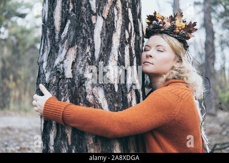 Young Caucasian woman hugging couronne à l'automne un pin dans la forêt avec les yeux fermés Banque D'Images