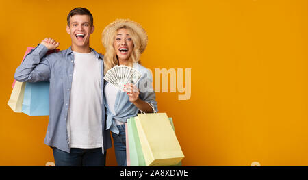 Young Couple Holding excité de sacs en papier et de tas de dollars Banque D'Images