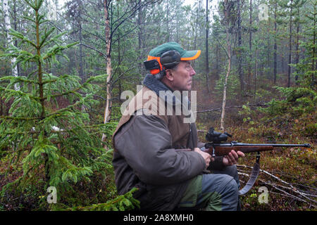 Moose hunter assis dans une forêt humide et brumeuse en tenant son fusil, photo du nord de la Suède. Banque D'Images