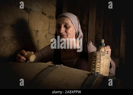 Femme en costume paysan médiéval contrôle de tonneaux de vin dans la cave d'un château médiéval authentique, libéré de la propriété en France Banque D'Images