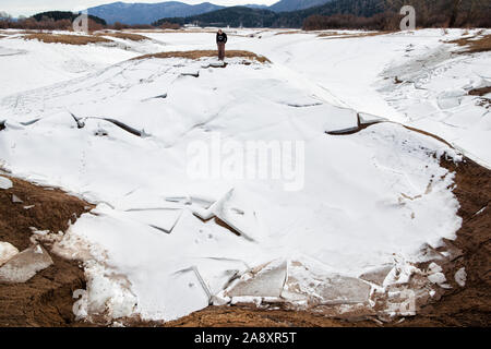 Un homme debout dans un champ gelé robuste avec plaques de glace s'est effondrée sur un lac asséché Cerknica en hiver. Banque D'Images