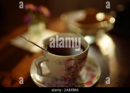 Tasse de thé noir avec une cuillère sur une soucoupe sur la table. Banque D'Images