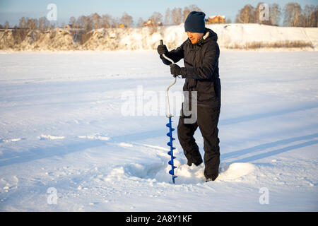 Un pêcheur perce un trou dans la glace pour attraper des poissons, Tom River à Kemerovo, Russie Banque D'Images