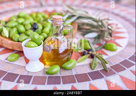 Olives vertes fraîches avec des branches et des feuilles. La récolte de saison en Italie. Bouteille d'huile d'olive et de baies sur une table en pierre Banque D'Images