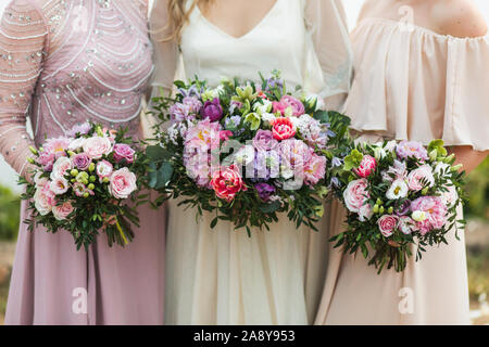 Trois demoiselles tenant dans les mains de beaux bouquets de fleurs avec du rouge, rose, violet, les pivoines, les roses, les tulipes. Style de mariage moderne et branché. Banque D'Images