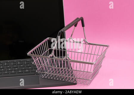 Internet shopping concept d'un ordinateur portable avec un mini panier panier repose sur le clavier isolés contre un fond rose Banque D'Images