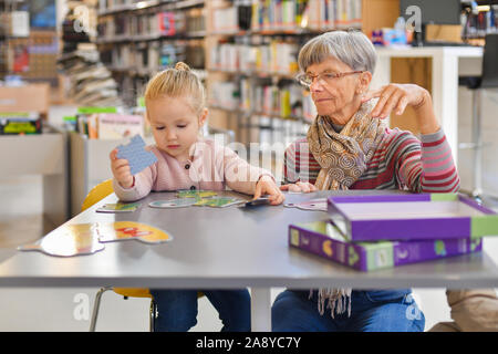 Petite-fille et grand-mère mettre ensemble un puzzle dans la bibliothèque de la ville Banque D'Images