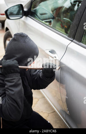 Un voleur habillé en noir tenue de biche à un chauffeur dans une voiture. Voleur de voiture, le vol de voiture concept. Banque D'Images