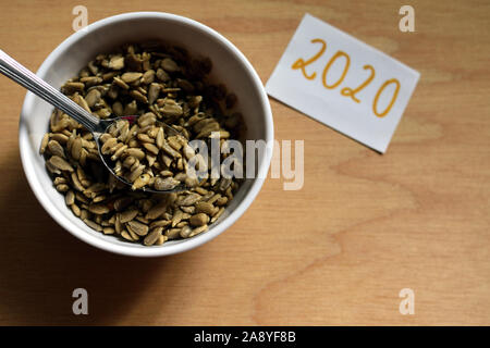 Graines de tournesol en blanc bol avec cuillère sur fond de bois et le numéro 2020 d'en haut Banque D'Images
