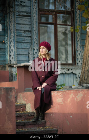 Dans un manteau femme assis sur le perron d'une vieille maison en bois. Banque D'Images