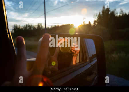 Self Portrait photographe prises avec un reflex numérique à partir du siège passager d'un SUV. Reflets de l'objectif et le coucher du soleil sont vus dans l'arrière-plan. Banque D'Images