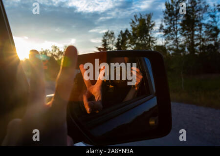 Photographe est à l'aide de son appareil photo reflex numérique pour faire un autoportrait à l'arrière, rétroviseur intérieur d'un SUV tout en voyageant sur le siège passager. Banque D'Images