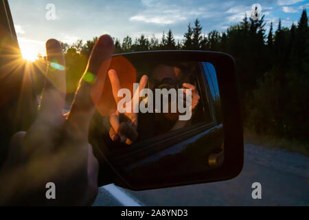 Homme photographe est à l'aide de son appareil photo reflex numérique pour faire un autoportrait à l'arrière, rétroviseur intérieur d'un SUV tout en voyageant Banque D'Images