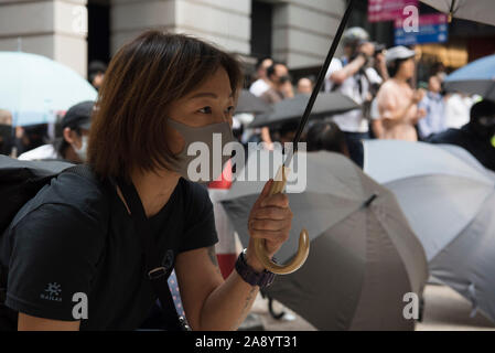 Manifestant observe approcher derrière un parapluie de la police pendant les manifestations.Des milliers d'employés de bureau et des manifestants masqués se heurtent à la police dans l'un des plus violents jours pour le pôle financier depuis le début des manifestations il y a cinq mois, un agent de police ont tiré sur un manifestant masqué et un autre homme a été aspergé d'essence et mis le feu. En dépit de la controversée LOI SUR L'extradition qui a suscité les protestations d'être formellement retirée, les manifestants continuent de demander aux Chef de la carrie Lam pour répondre à leurs demandes restantes qui inclut le suffrage universel, un organisme indépendant inve Banque D'Images