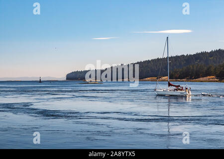 Sous un ciel presque sans nuages, un voilier motors par tourbillons de marée au passage Gabriola, Colombie-Britannique (Valdes Island en arrière-plan). Banque D'Images