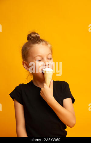 Petite danseuse dans un maillot aux yeux clos mange la crème glacée dans un studio sur un fond jaune Banque D'Images