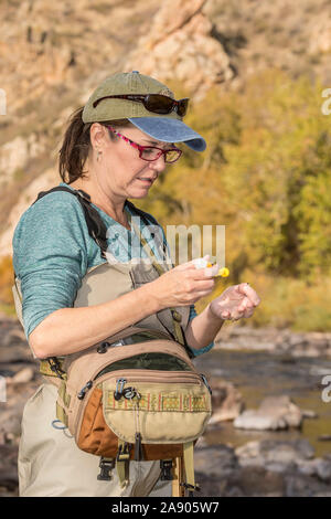 Une femme ajoute à son pansement de mouche sèche fly en préparation de la pêche sur une journée d'automne ensoleillée le long de la Powder River, dans le Colorado. Banque D'Images